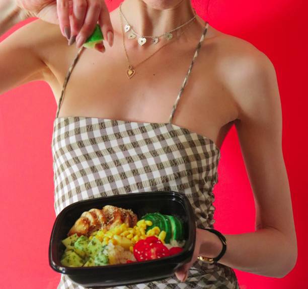 istock Slim female model squeezing a lemon on vegetable salad, on isolated pink background 1487270706