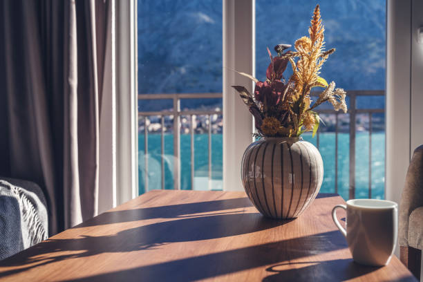 Vase of dried flowers on a wooden table in the living room overlooking the lake and mountains. sunny day stock photo