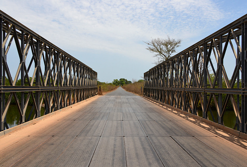 Charobrique, Cacheu Region, Guinea-Bissau: colonial truss bridge with steel deck over the Costa River, a tributary of the Cacheu River, with mangroves on the riverbank (called 'tarrafes') - diminishing perspective view north along the R1 road.