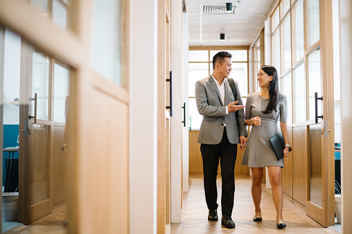 Asian Chinese businessman and businesswoman walking in corridor.