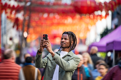 Black male in his 30s using a smartphone to photograph red paper lantern decorations for the Chinese New Year celebrations in Gerrad Street, London.