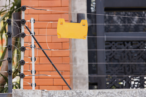 high voltage security fence on house wall with blank yellow plastice sign.