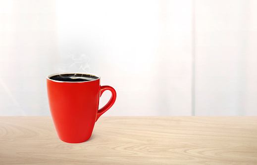 Hot coffee in red mug on wooden table There is a white mirror in the background.