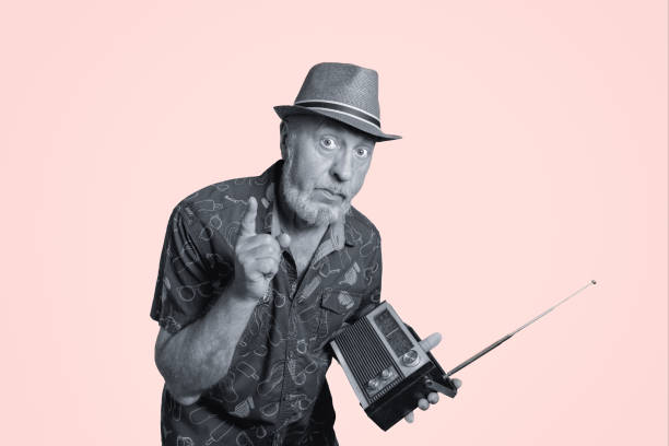 джентльмен в шляпе слушает портативный радиоприемник с антенной. ретро-концепция. черно-белый портрет на розовом фоне - pink and white radio стоковые фото и изображения