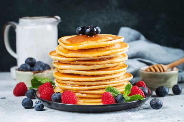 istock Delicious pancakes, with fresh blueberries, raspberry and maple syrup or honey on a dark background 1487279095