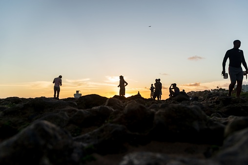 Salvador, Brazil – December 12, 2021: Fishermen fishing on top of the rocks at Rio Vermelho beach in Salvador, Bahia.