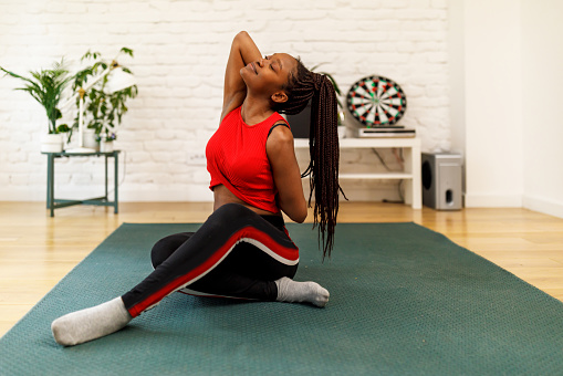 A young athlete is preparing for a workout at home while stretching her body.