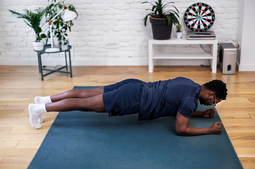 A male athlete of African-American ethnicity is exercising in the living room by doing push-ups.