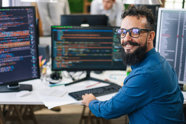 istock Portrait of smiling IT Programmer sitting near Desktop Computers. Male Specialist Creating Innovative Software. Engineer Developing App, Program, Video Game. Writing Code in Terminal 1487286241