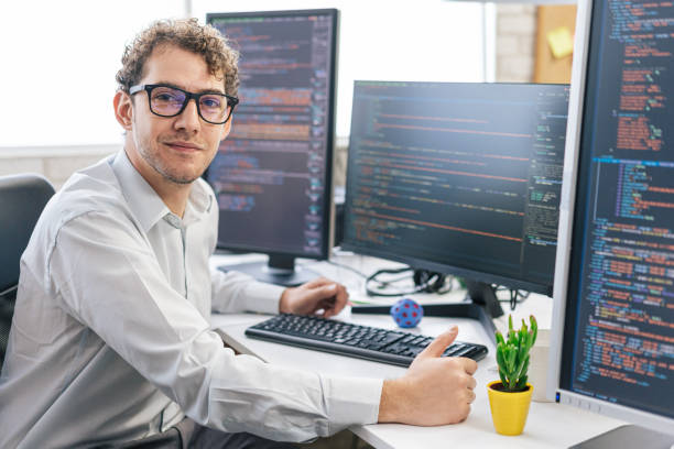istock Portrait of young smiling female programmer, sitting on her desk with computers in an IT office 1487286434