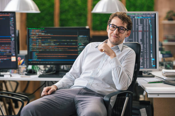 istock Portrait of smiling IT Programmer sitting near Desktop Computers. Male Specialist Creating Innovative Software. Engineer Developing App, Program, Video Game. Writing Code in Terminal 1487286783