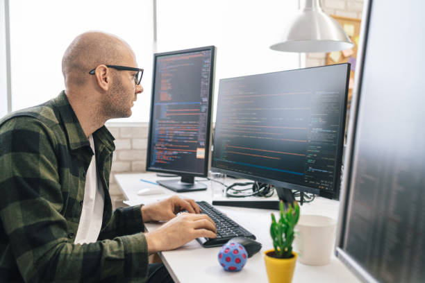 istock Portrait of smiling IT Programmer sitting near Desktop Computers. Male Specialist Creating Innovative Software. Engineer Developing App, Program, Video Game. Writing Code in Terminal 1487286791