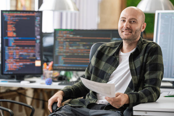 istock Portrait of smiling IT Programmer sitting near Desktop Computers. Male Specialist Creating Innovative Software. Engineer Developing App, Program, Video Game. Writing Code in Terminal 1487286798