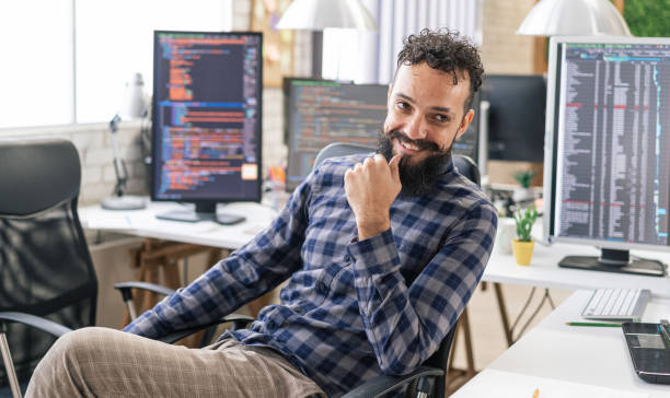 istock Portrait of smiling IT Programmer sitting near Desktop Computers. Male Specialist Creating Innovative Software. Engineer Developing App, Program, Video Game. Writing Code in Terminal 1487286855