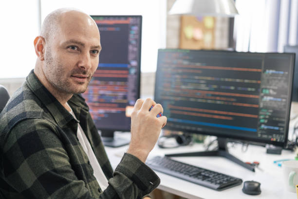 istock Portrait of smiling IT Programmer sitting near Desktop Computers. Male Specialist Creating Innovative Software. Engineer Developing App, Program, Video Game. Writing Code in Terminal 1487286864
