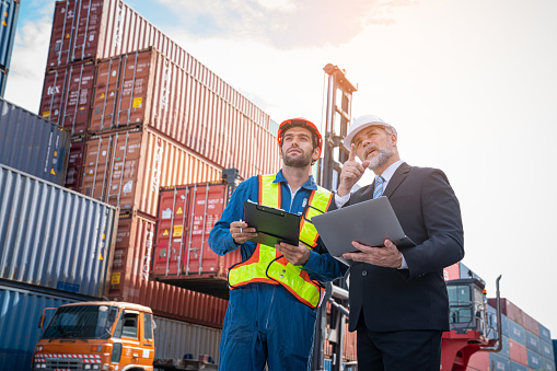 Container yard manager with safety hat talking to foreman about the goods inside the warehouse, Logistics business, Import and export concept.