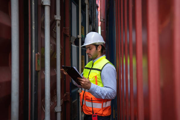 Male Industrial Engineer in White Hard Hat checking container at container yard warehouse. stock photo