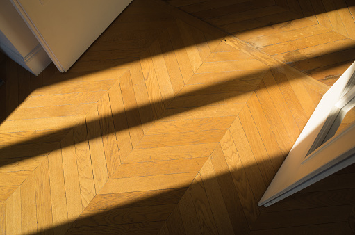 Solid hardwood parquet in sunlight in Haussmannien building in Paris, France; chevron pattern.