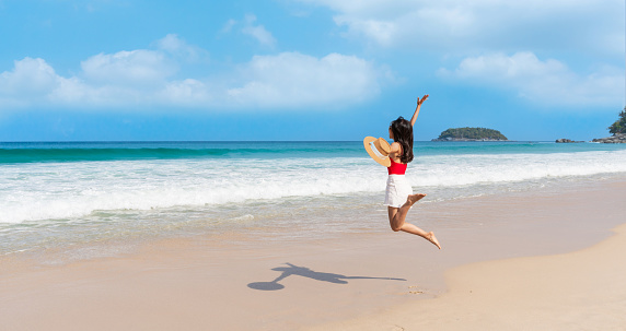 Happy young Asian female relax smile around beautiful tropical sea beach ocean with white cloud on blue sky in travel vacation. Summer and holiday concept. Copy space