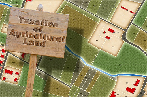 Property tax and costs on land for agricultural use - concept with an imaginary cadastral map and information placard