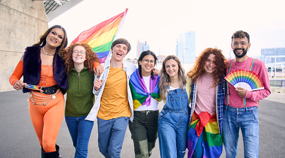 Group of young cheerful friends strolling together on day of gay pride parade in city. People LGBT community pose hugging looking smiling at camera outdoor. Generation z and sexual liberation.
