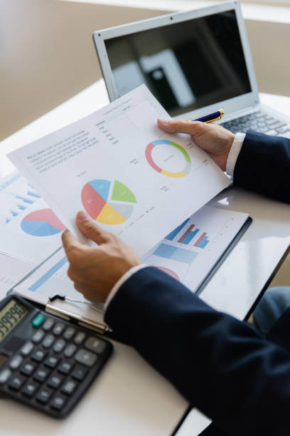 istock Asian businessman working at office with laptop, tablet and graph data sheet on his desk. 1487296086