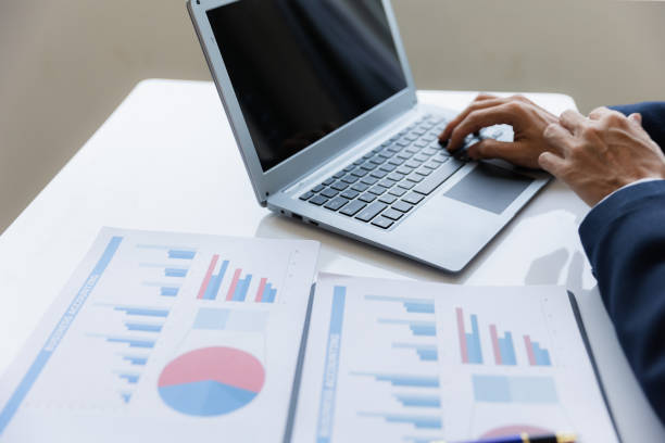 istock Asian businessman working at office with laptop, tablet and graph data sheet on his desk. 1487296092