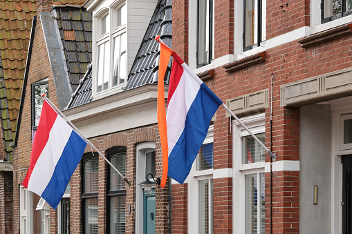 Dutch flags with orange streamers waving in the wind in a typical dutch street on Koningsdag in the Netherlands. King's day is a national holiday in the Kingdom of the Netherlands
