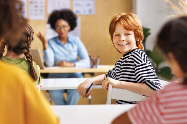istock Cheerful redhead teen boy smiling at camera during lesson  in class 1487298446