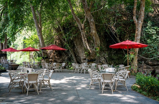 An outdoor cafe with a variety of tables and chairs in the shade, allowing patrons to enjoy their meals in a pleasant atmosphere