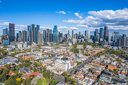 Not the usual cityscape view of Melbourne: aerial view of Melbourne's growing wide cluster of CBD skyscrapers taken from North Melbourne showing the contrast of old and new architecture in the foreground. Tree-lined streets low-rise buildings and parklands in established older suburb.