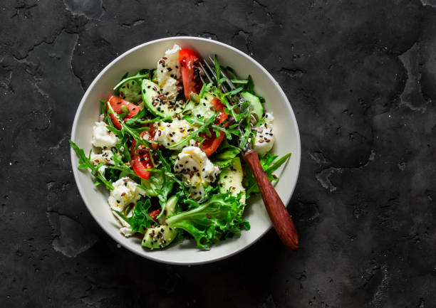 istock Simple salad with fresh vegetables, avocado and mozzarella on a dark background, top view 1487302905
