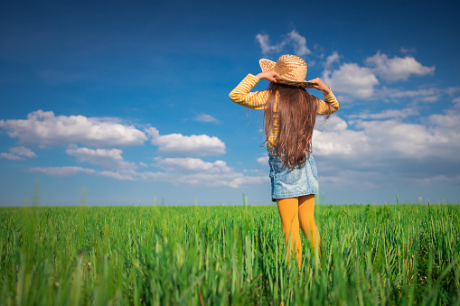 Green wheat field landscape and happy farmer girl playing with straw hat