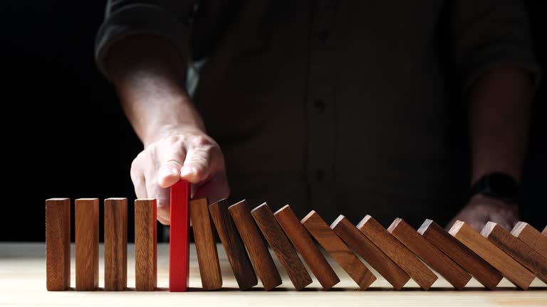 Businessman hand stopping wooden domino business crisis effect or risk protection on dark background. Concept of Risk, Risk Management, Assessment, Business, Crisis, Financial, Planning, Economic