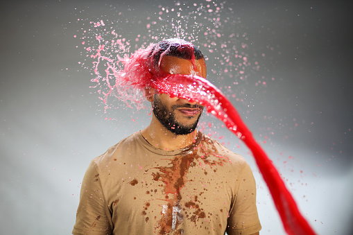 Mature man being splashed with colored water. Red color.