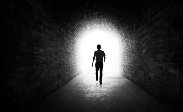 Young man walking through a dark tunnel Young man walking through a dark tunnel light at the end of the tunnel stock pictures, royalty-free photos & images