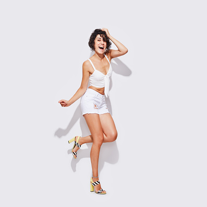 Full length shot of young slim female in denim shorts standing, on white background