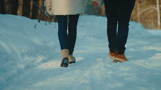 loving couple walking in winter in park or forest, back closeup of feet on snowed path, 4K, Prores