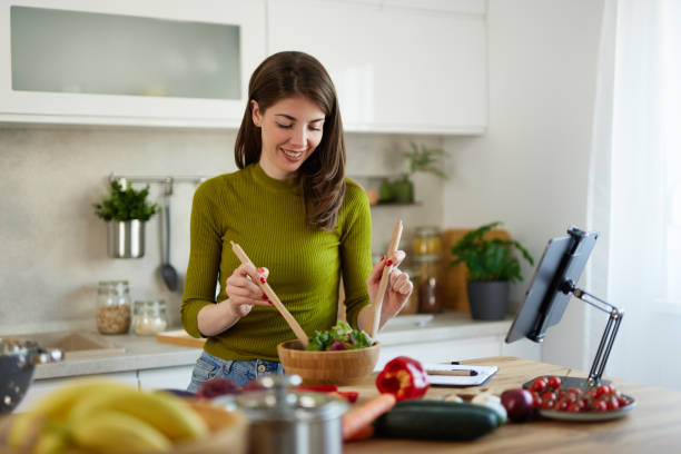 istock Young woman standing in the kitchen making a salad using online recipe 1487309318