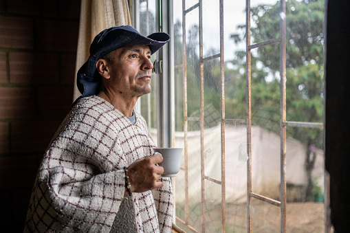 Mature man contemplating looking through the window in a farm home