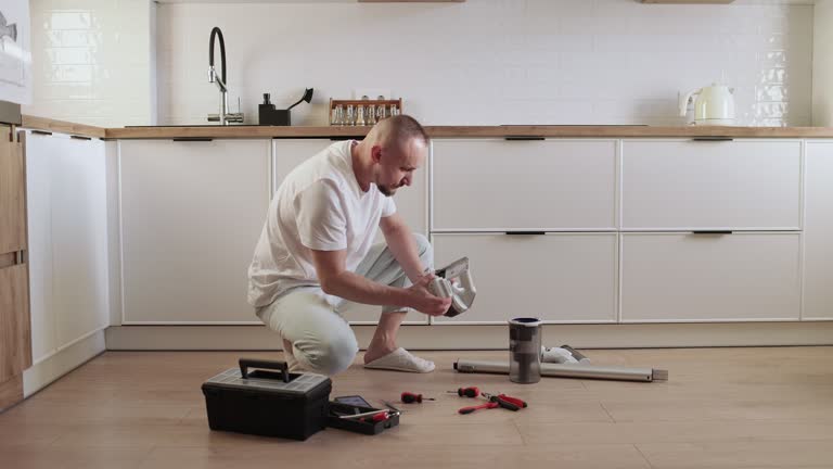 Housework and technology concept. Man repairing, fixing, cleaning or replacement of parts wireless vacuum cleaner at the kitchen floor at home. Concept of maintenance modern home appliance