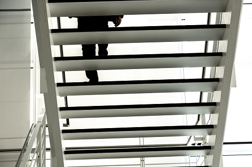 Silhouette of legs and feet of a man climbing up the black steps of a modern open staircase with white banister