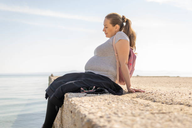Pregnant woman sitting on a pier relaxing and enjoying fresh sea air