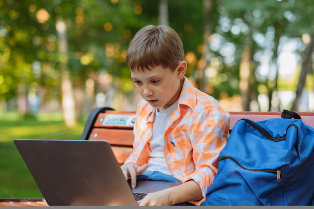 istock cute caucasian boy sitting on bench in park with laptop computer. Black screen 1487314787