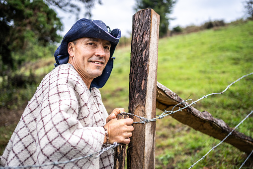 Portrait of a mature farmer opening or closing cattle barbed wire gate in the farm