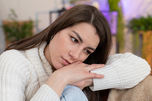 Sad lonely young woman sitting at home room looks pensive thinks over life concerns or unrequited love suffers from unfair situation. Alone girl problem break up, depressed feeling bad annoyed burnout