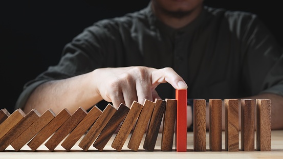 Businessman hand stopping wooden domino business crisis effect or risk protection on dark background. Concept of Risk, Risk Management, Assessment, Business, Crisis, Financial, Planning, Economic