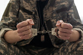 A handcuffed soldier behind the bars against a black background. Concept: court martial, refusal to mobilize, crime in the army.