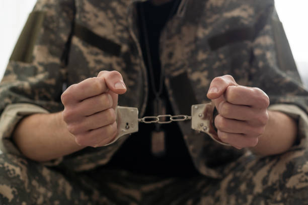 A handcuffed soldier behind the bars against a black background. Concept: court martial, refusal to mobilize, crime in the army. stock photo