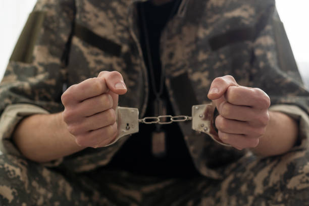 A handcuffed soldier behind the bars against a black background. Concept: court martial, refusal to mobilize, crime in the army. A handcuffed soldier behind the bars against a black background. Concept: court martial, refusal to mobilize, crime in the army stuck stock pictures, royalty-free photos & images